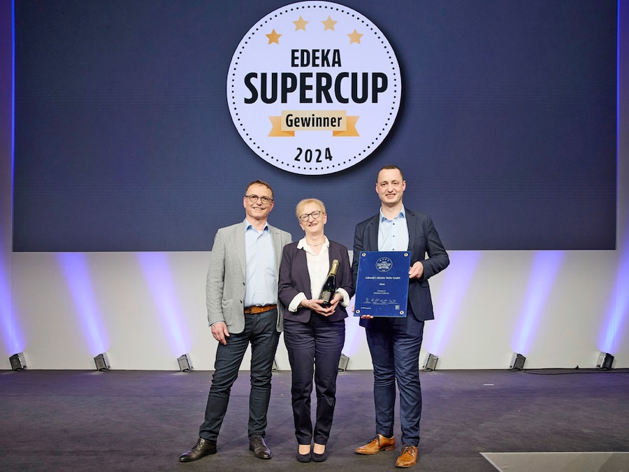 Eine Frau und zwei Männer zeigen ihreSieger-Urkunde auf einer Bühne vor einer Leinwand mit dem Text EDEKA Supercup Gewinner