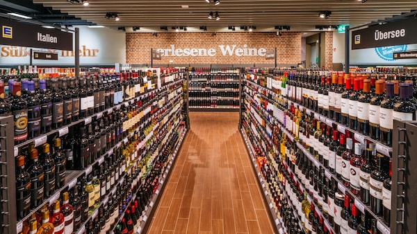 Weinabteilung: Regale mit Weinflaschen gefüllt, Blick nach hinten an der Wand. Über dem Regal quer steht 