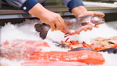 Nahaufnahme einer Bedientheke, Hände präsentieren einen Fisch.
