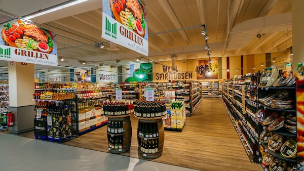 Marktkauf-Markt: Blick in die Weinabteilung mit Weinregalen, Holzfässern, Holzboden und Holzdecke.